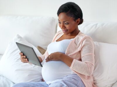 Pregnant woman on couch holding a tablet