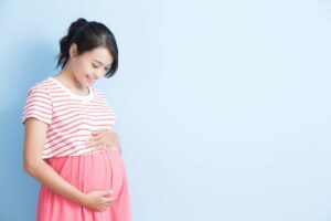 Woman with dark hair in pink striped top and pink skirt holds her pregnant belly