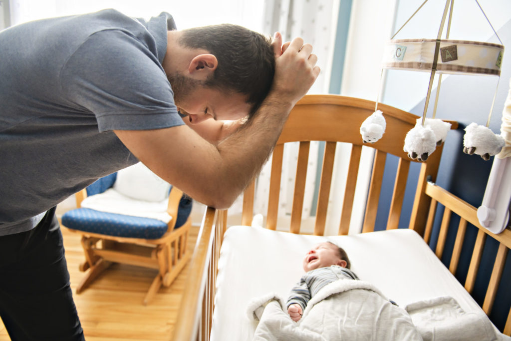 frustrated-father-leaning-over-baby's-crib-with-head-in-his-hands
