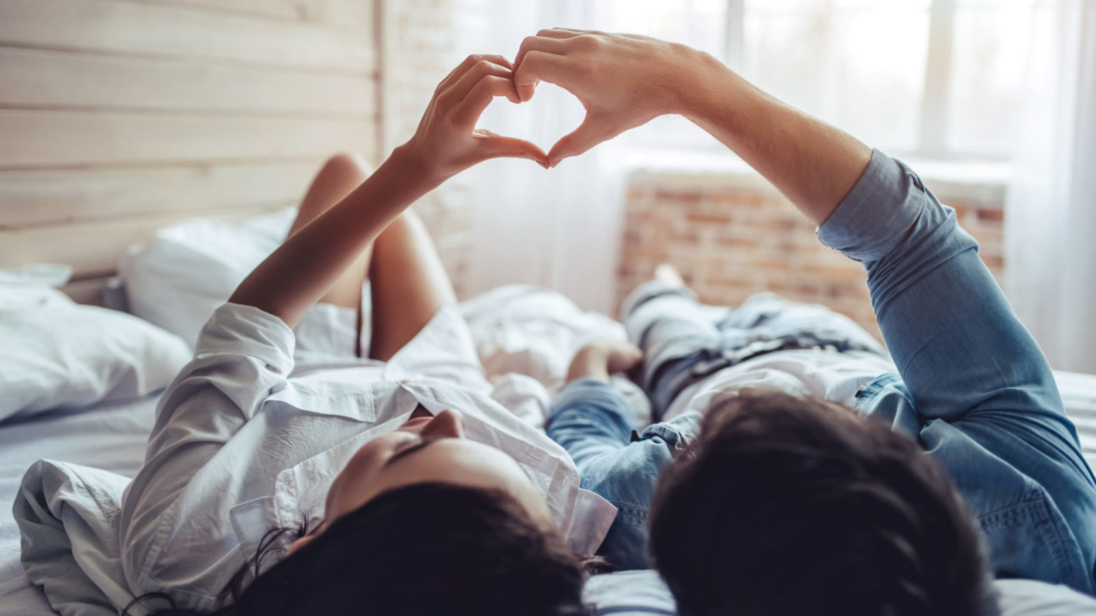 Couple-laying-on-bed-making-heart-shape-with-hands-trying-to-get-pregnant